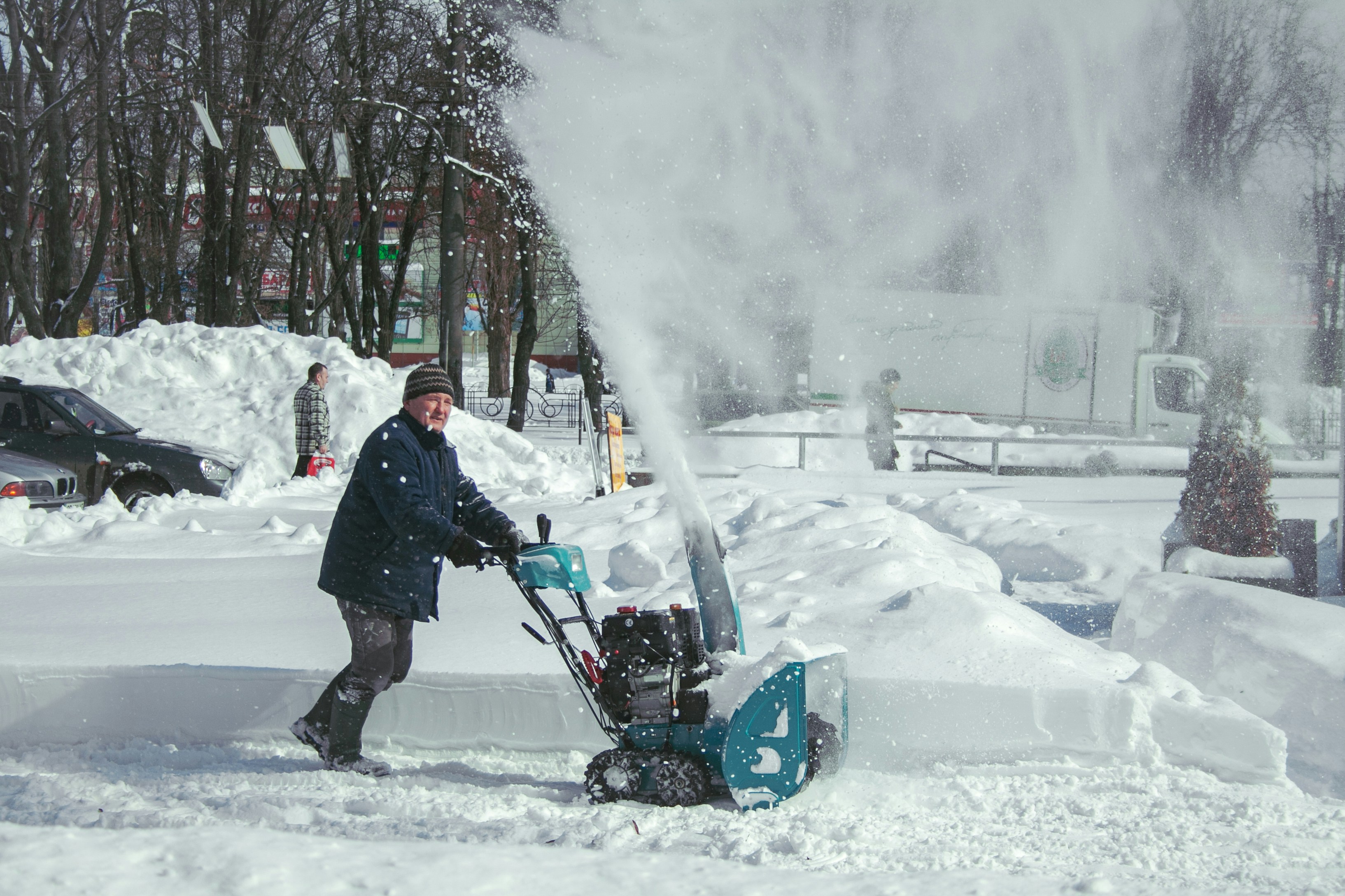 Mann bedient eine Schneefräse beim Räumen eines verschneiten Parkplatzes im Winter