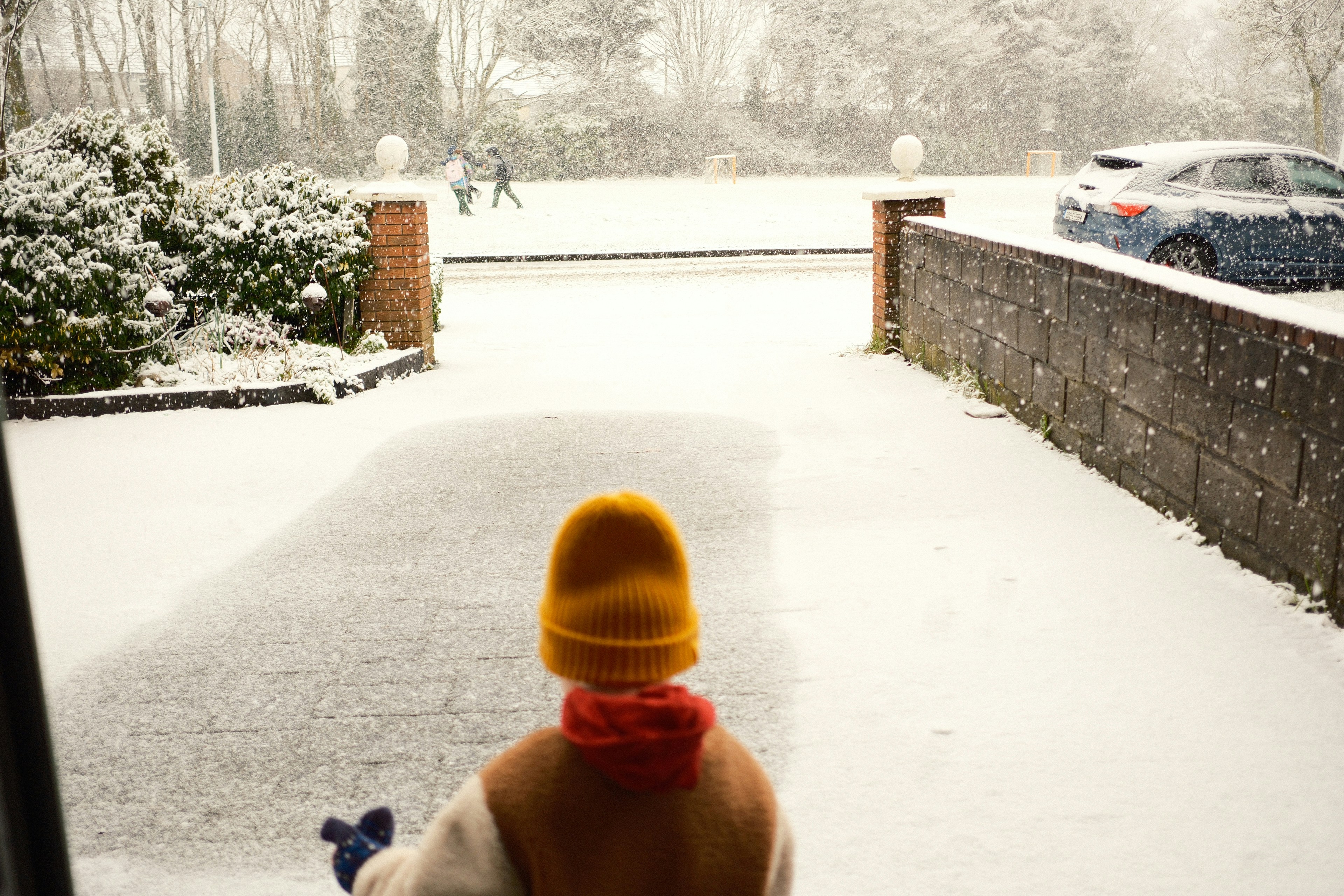 Kind mit gelber Wintermütze blickt auf verschneite Einfahrt und Straße