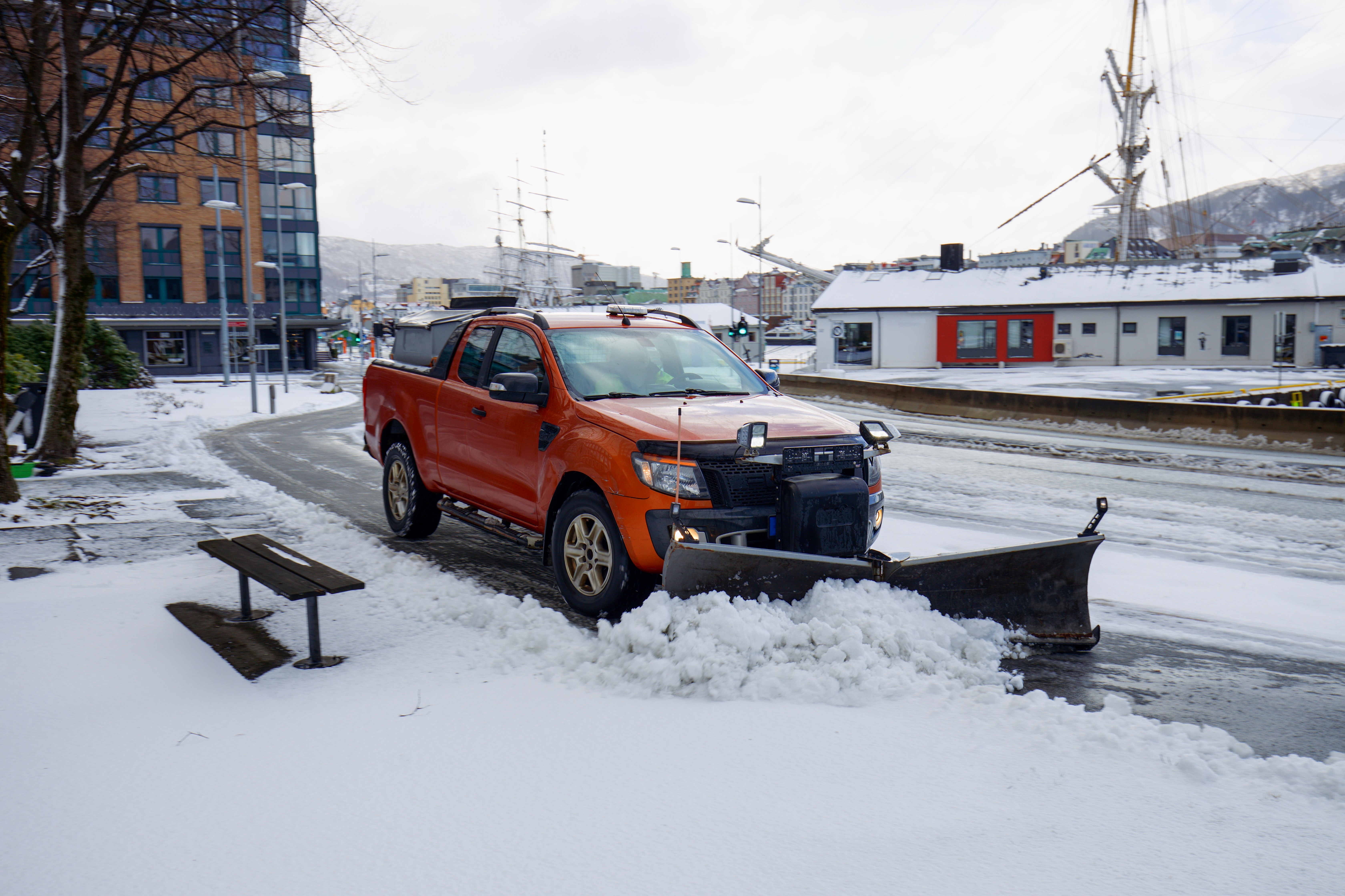 Orangefarbener Pickup-Truck mit Schneepflug räumt verschneite Stadtstraße im Winter