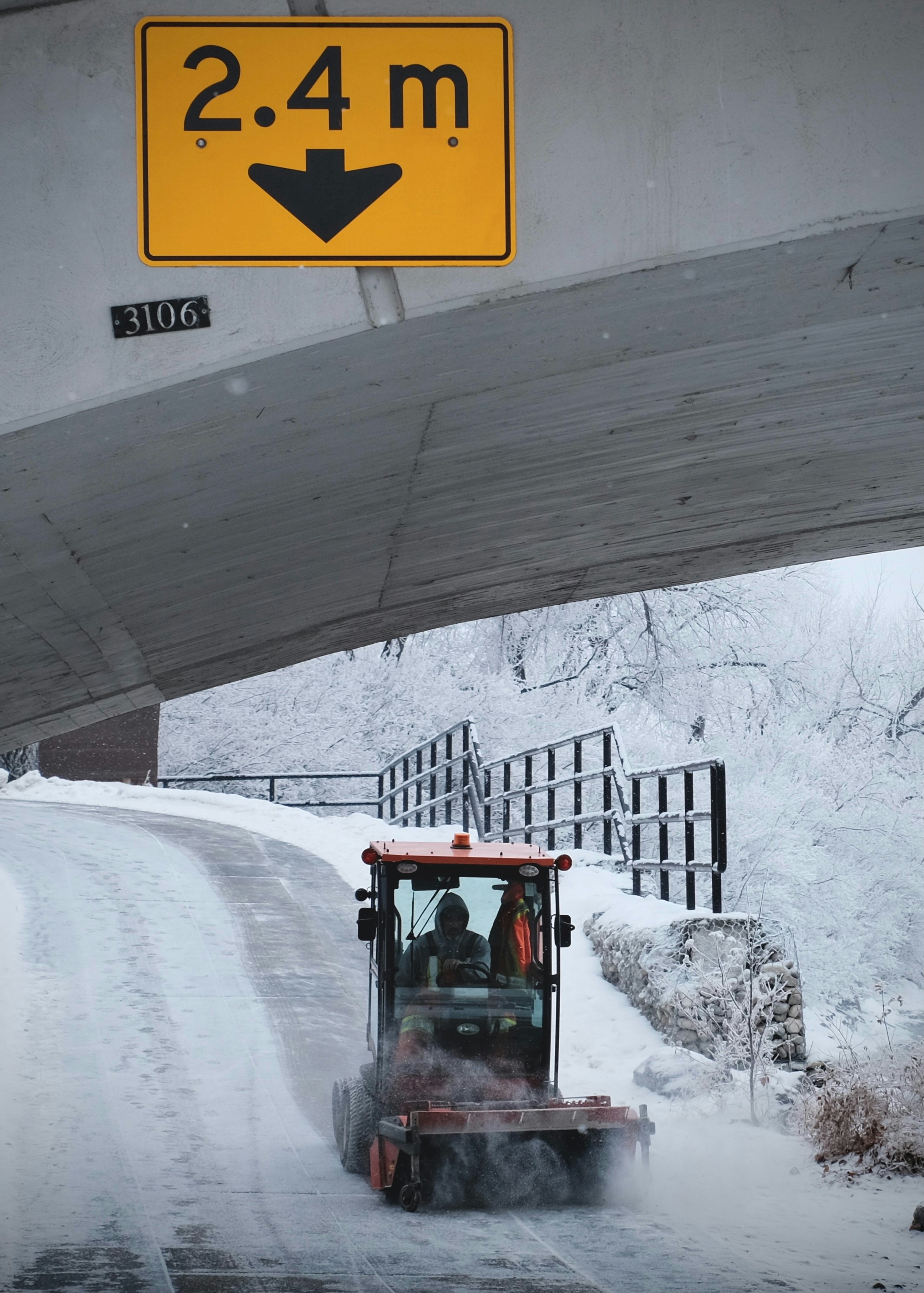 Kleiner Schneepflug räumt vereiste Straße unter Brücke mit Höhenbegrenzungsschild 2,4 Meter