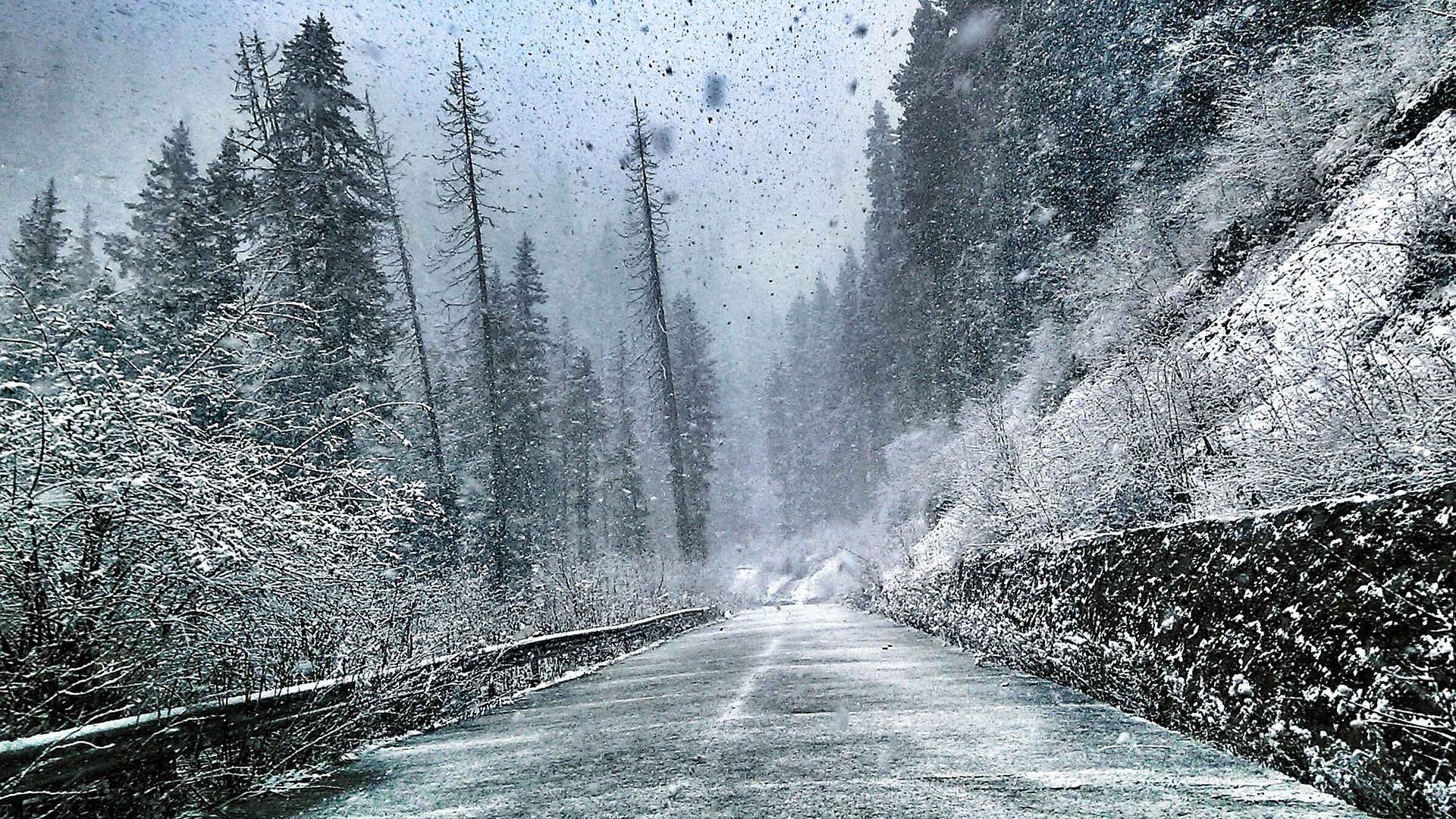 Verschneite Bergstraße bei starkem Schneefall, Blick durch eine beschlagene Autoscheibe