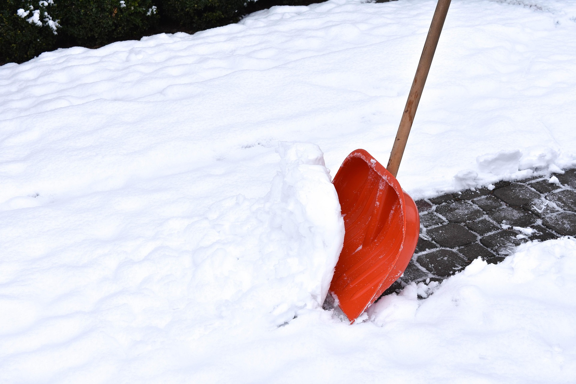 Rote Schneeschaufel steckt im Schnee neben geräumtem Gehweg