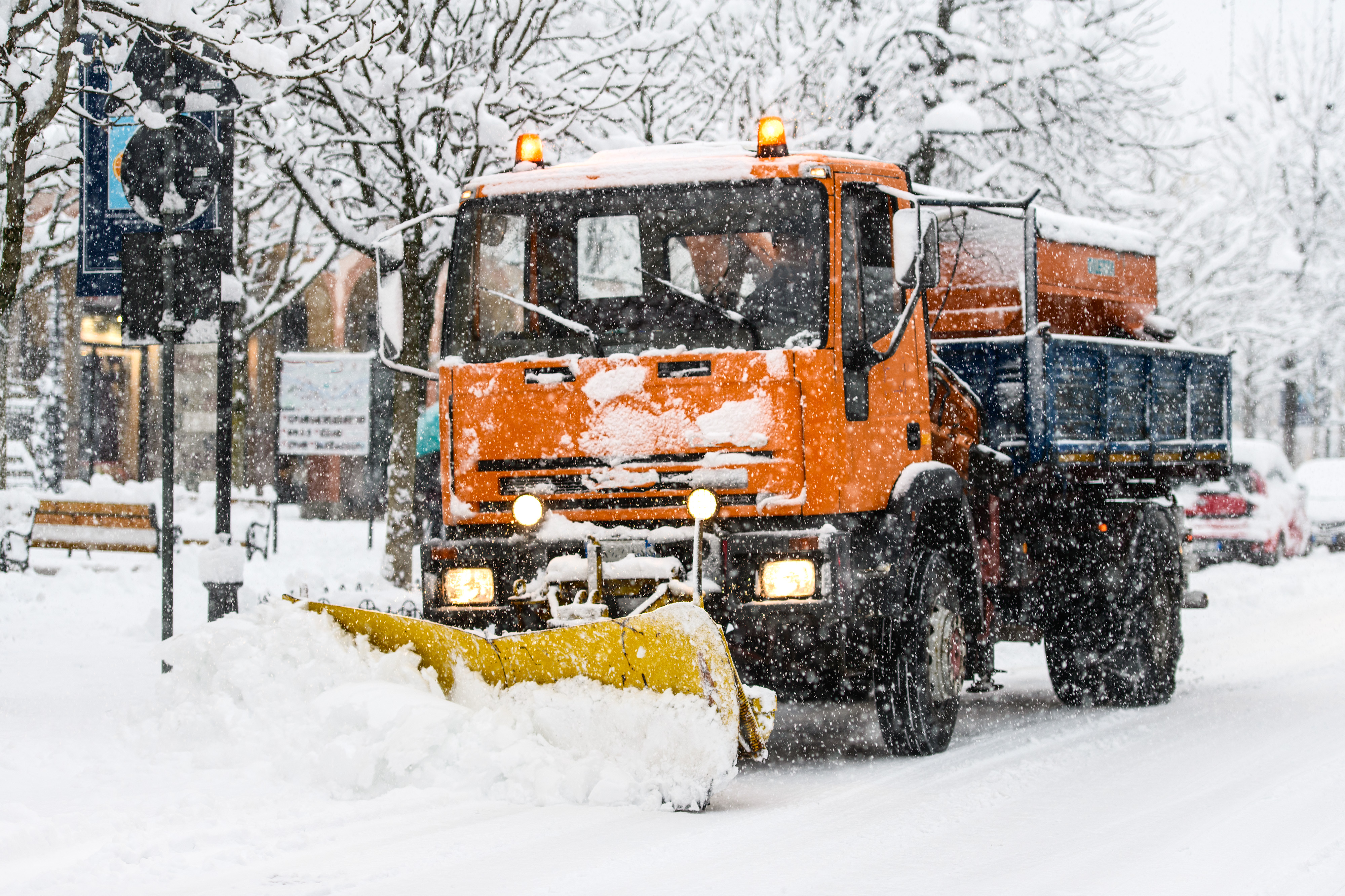 Orangefarbener Räumfahrzeug mit gelbem Schneepflug räumt Straße bei starkem Schneefall