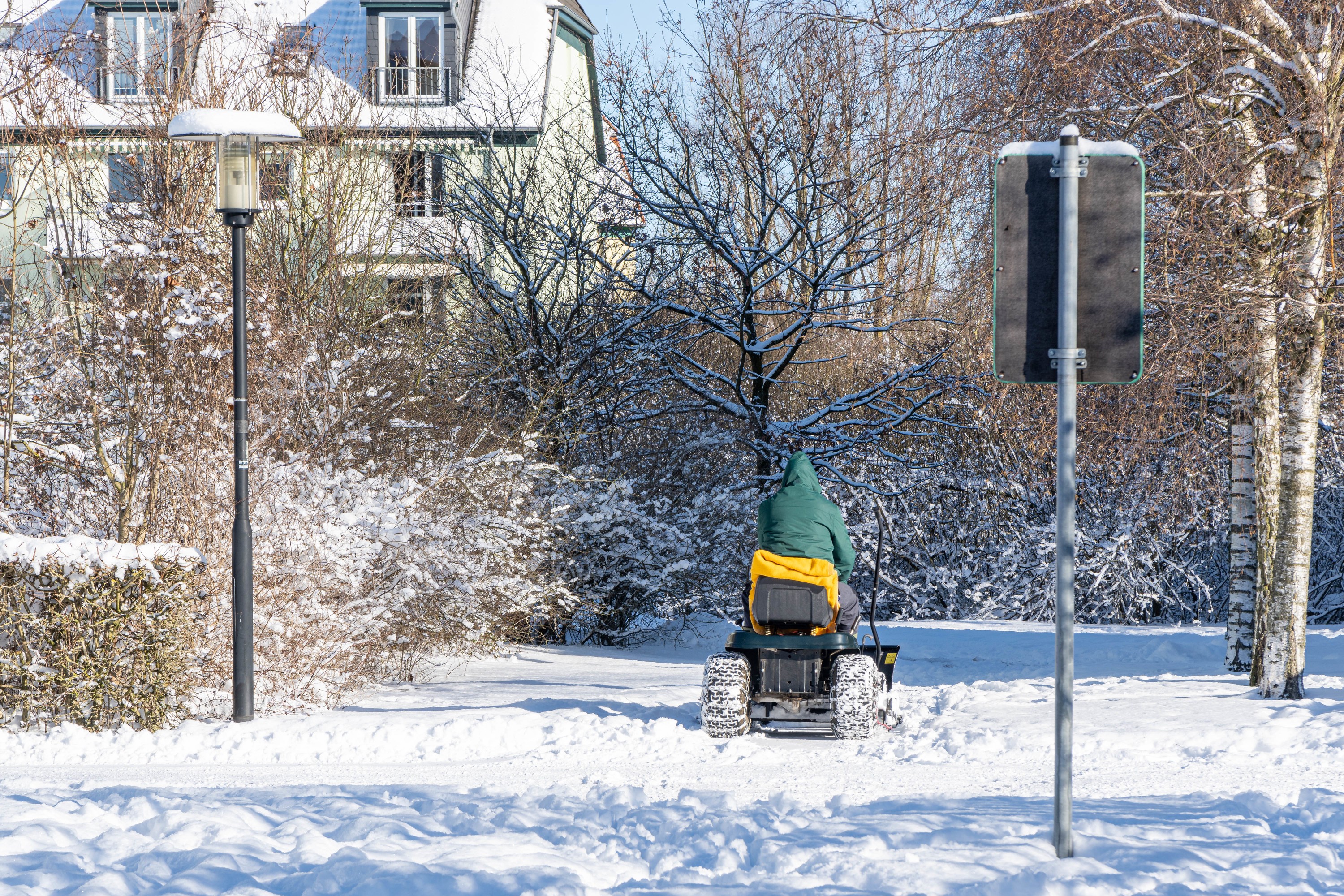 Mitarbeiter fährt mit Aufsitz-Schneefräse über einen winterlichen Gehweg zur Schneeräumung