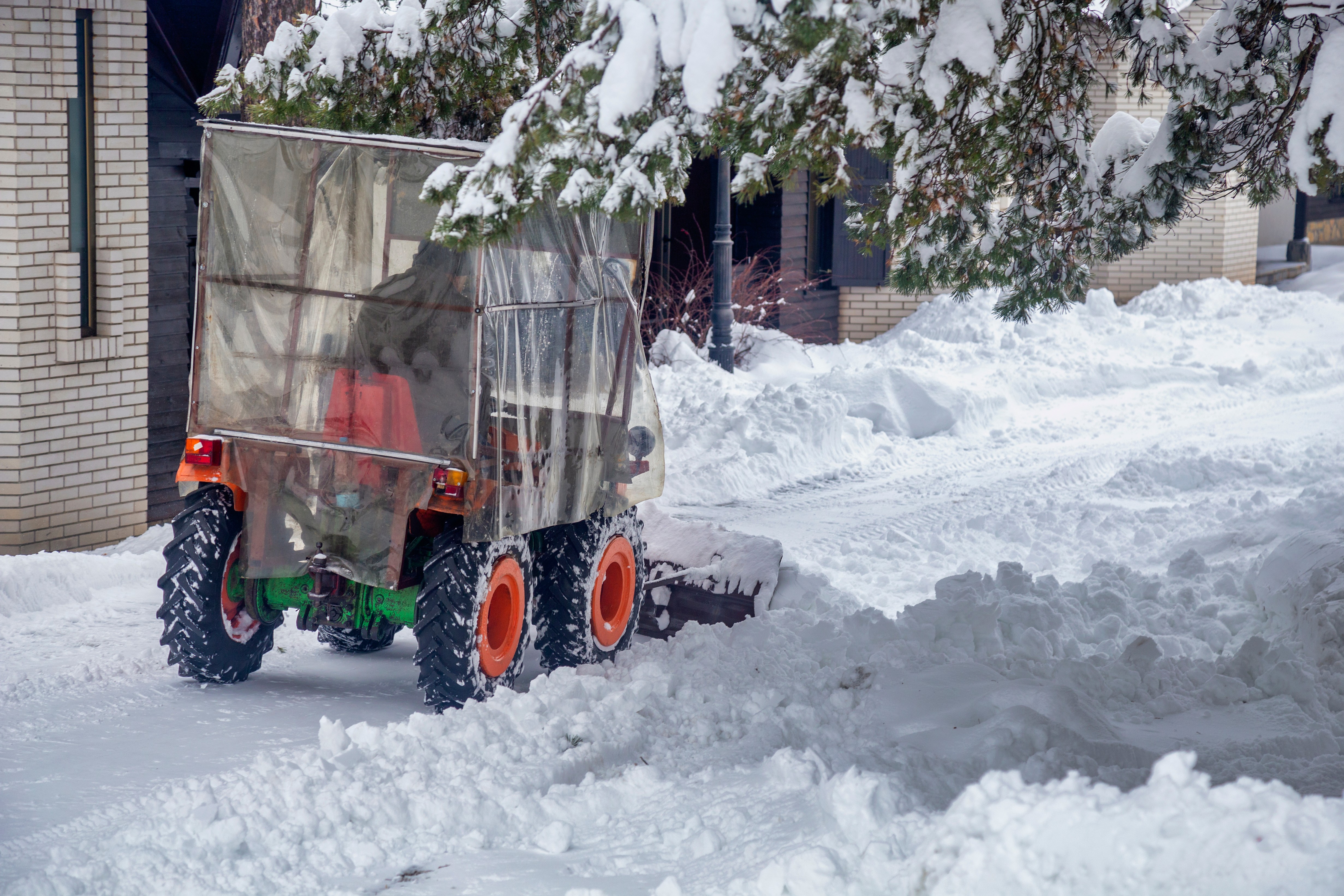 Kleintraktor mit Schneeschild räumt schneebedeckte Einfahrt vor einem Wohnhaus
