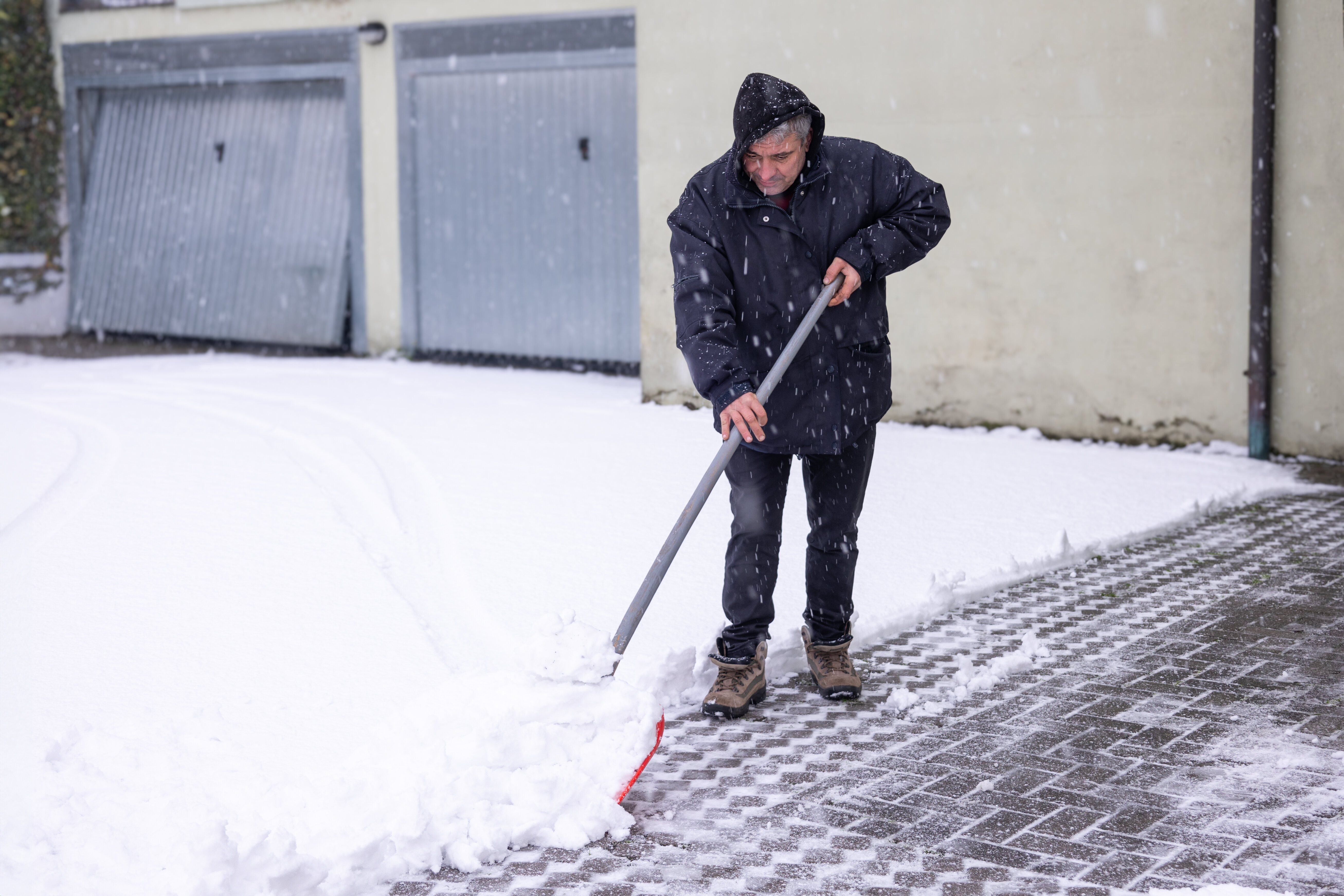 Winterdienst am Mehrfamilienhaus – Bewohner schaufelt Schnee vor Garageneinfahrt