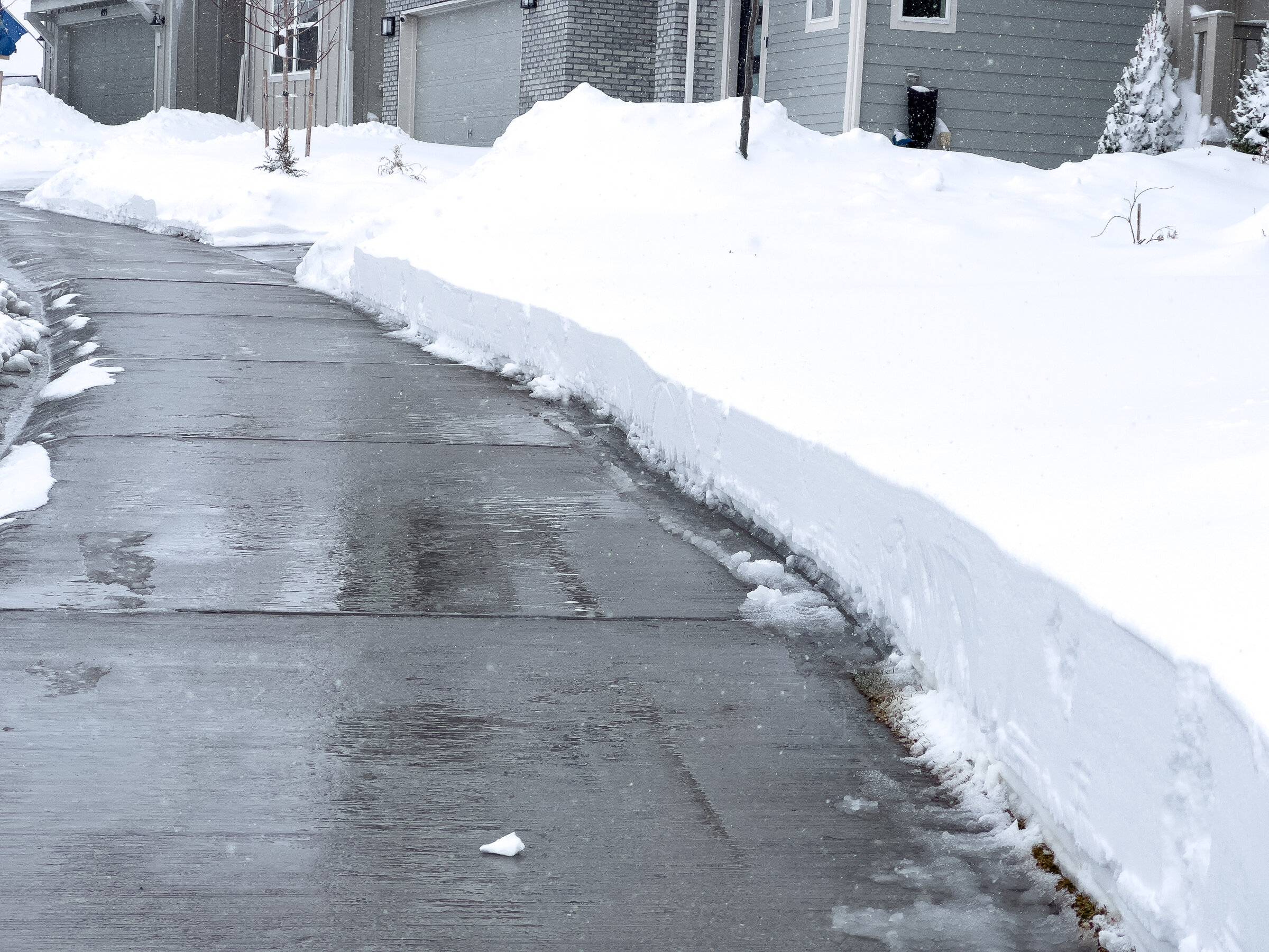 Geräumte, schneefreie Einfahrt neben hohen Schneehaufen vor Wohnhaus