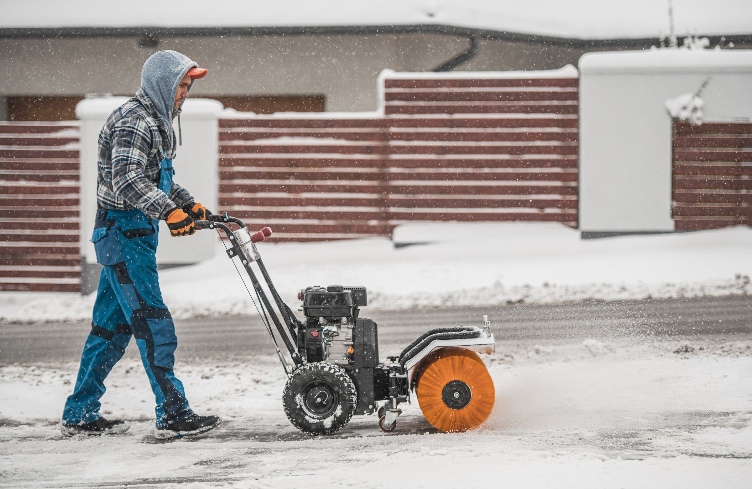 Mann räumt mit einer Kehrmaschine Schnee von der Einfahrt