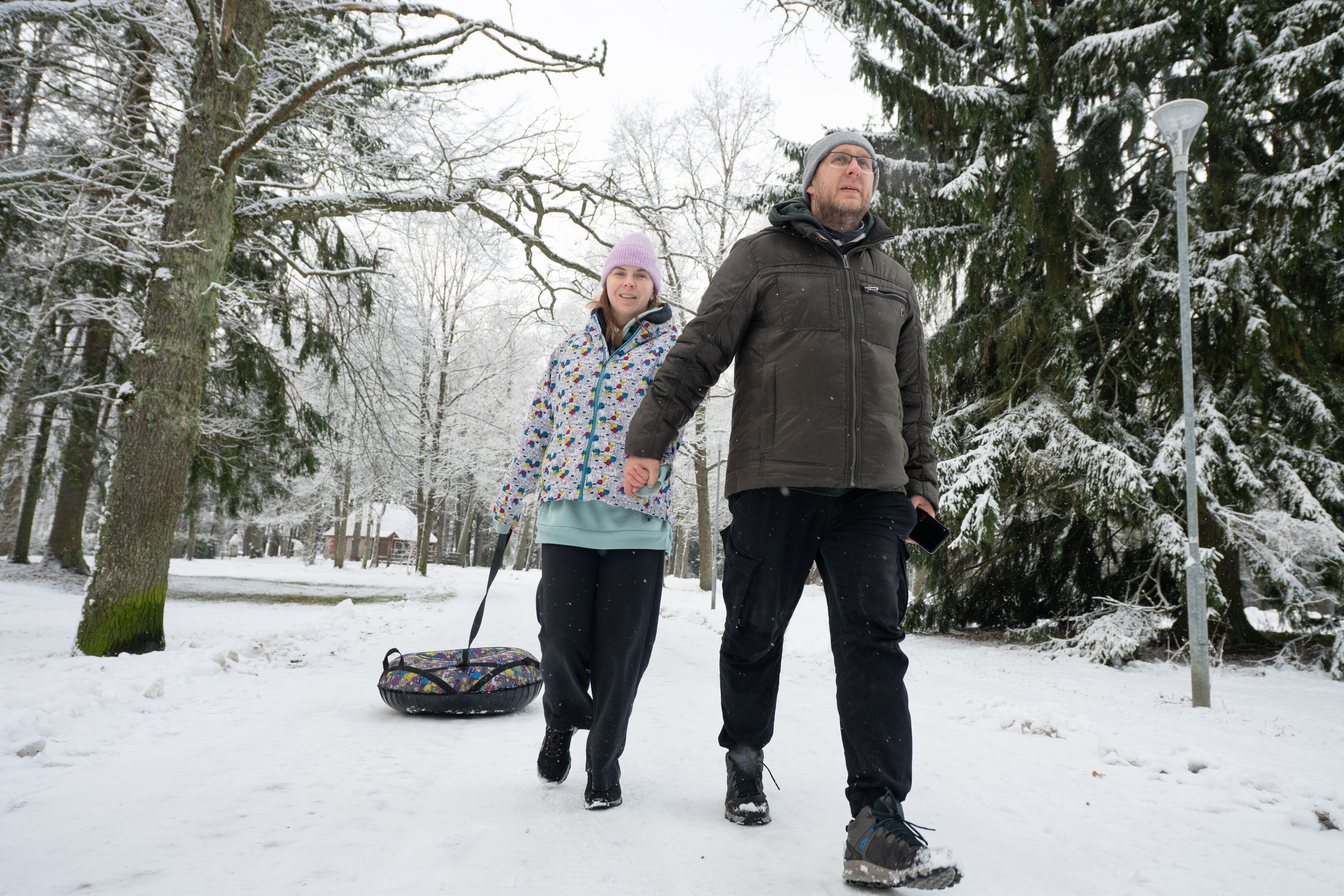 Paar hält Händchen und zieht einen Schneeschlauch-Schlitten durch einen schneebedeckten Winterwald