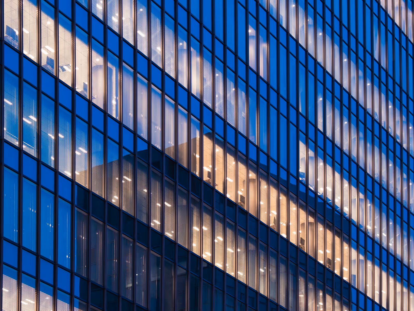 Close-up of office building windows with lights on during dusk reflecting blue sky.
