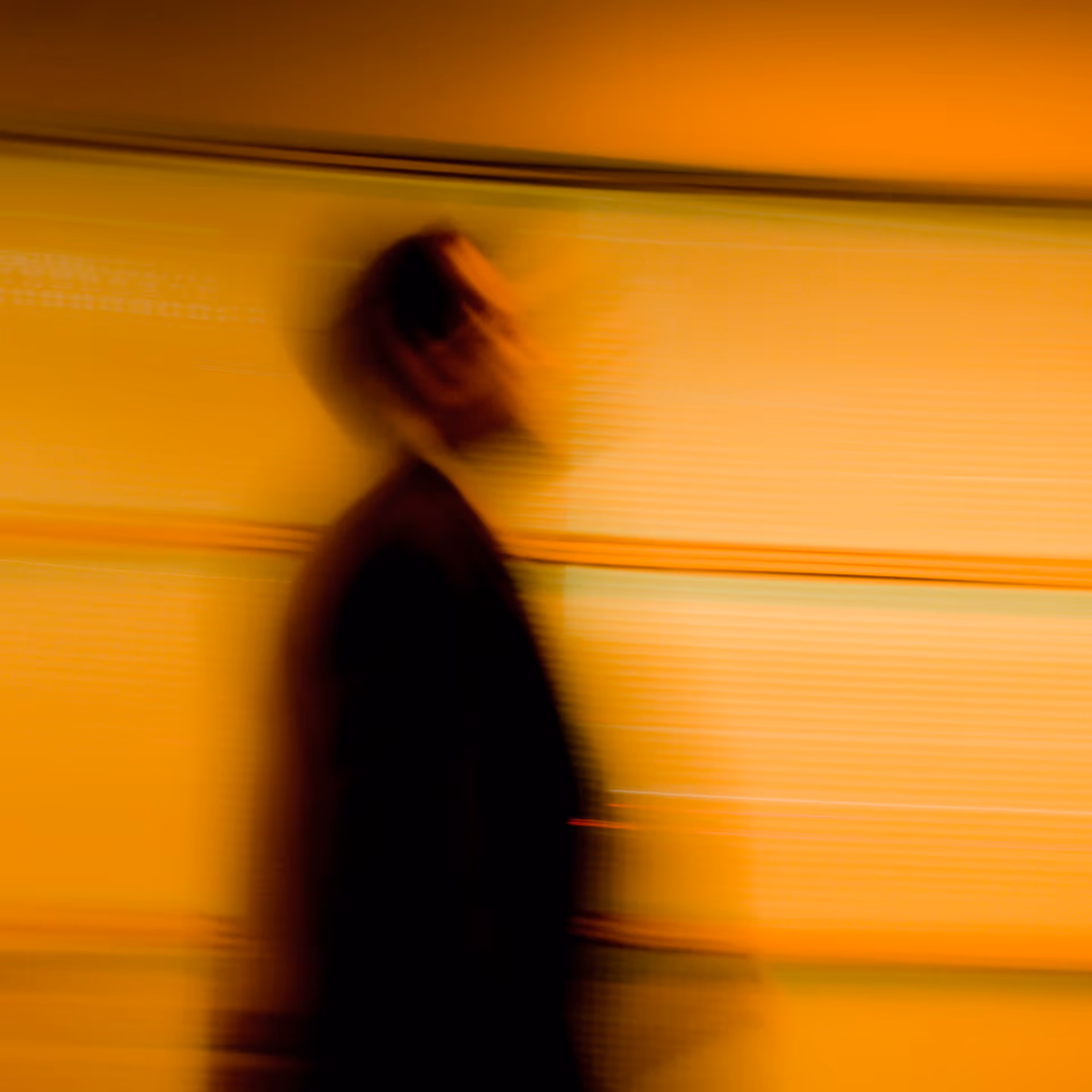 Blurred silhouette of a person against an orange-yellow background.