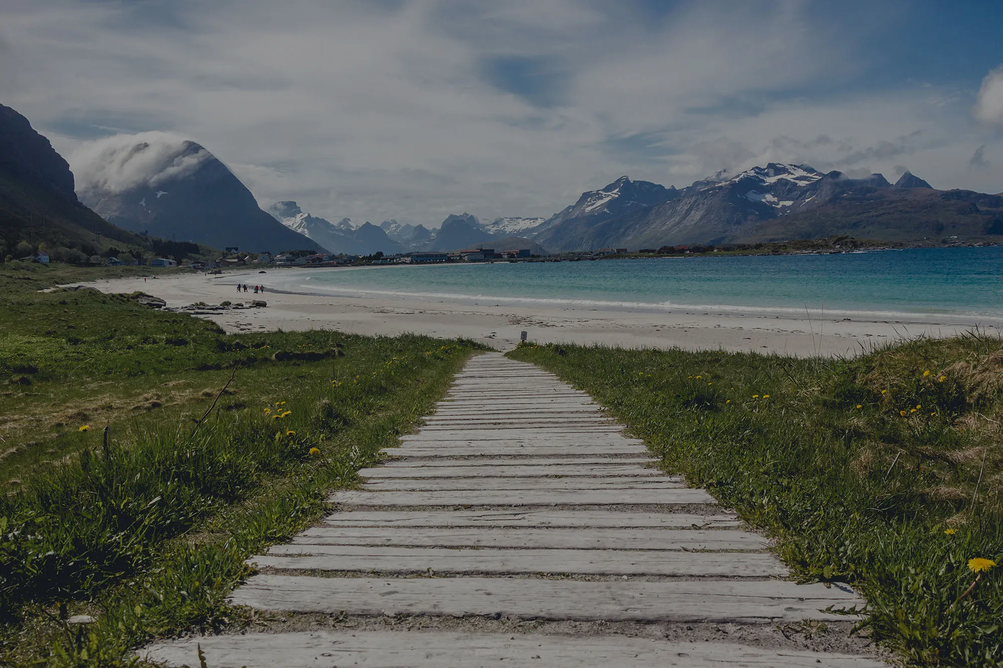 Scenic Nordic beach with a wooden pathway leading towards mountains under a cloudy sky