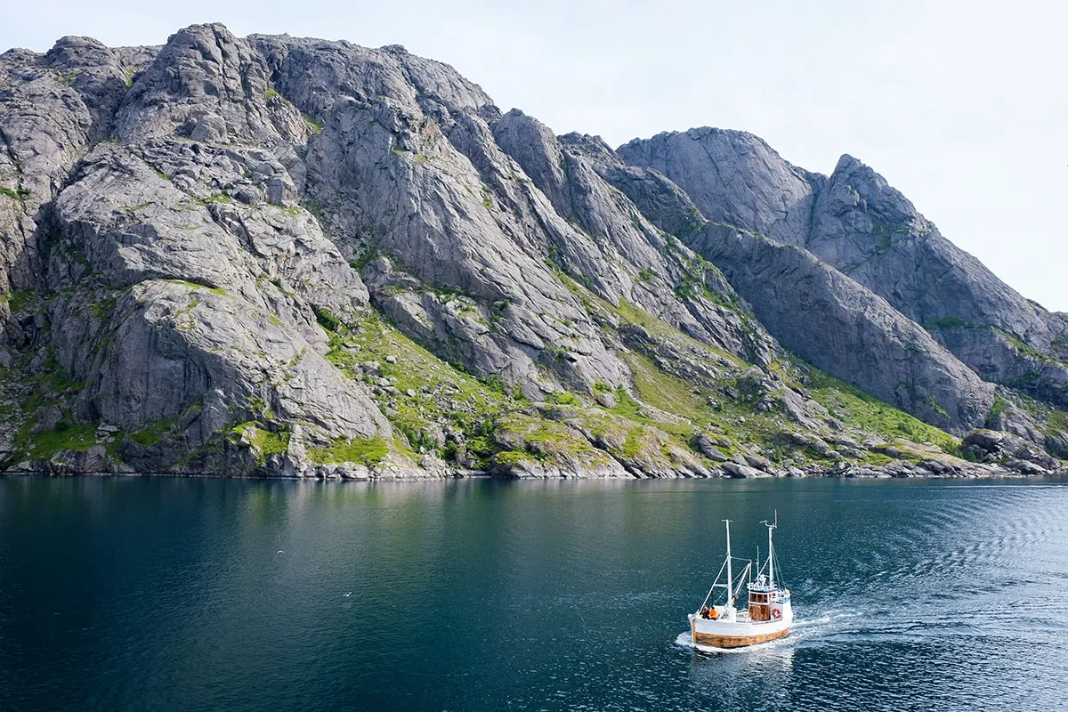 Small fishing boat in a fjord beneath granite cliffs