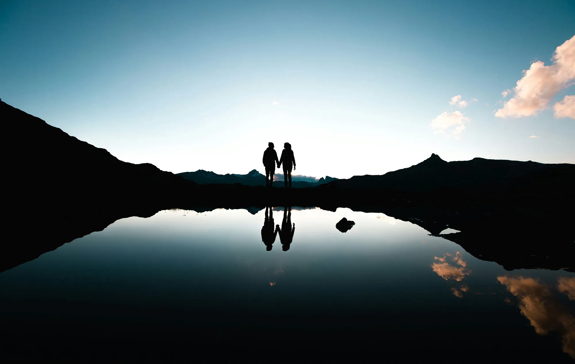 Travellers silhouetted beside a mountain lake