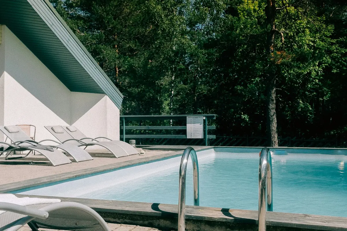 Outdoor pool and sun loungers beside a pine forest