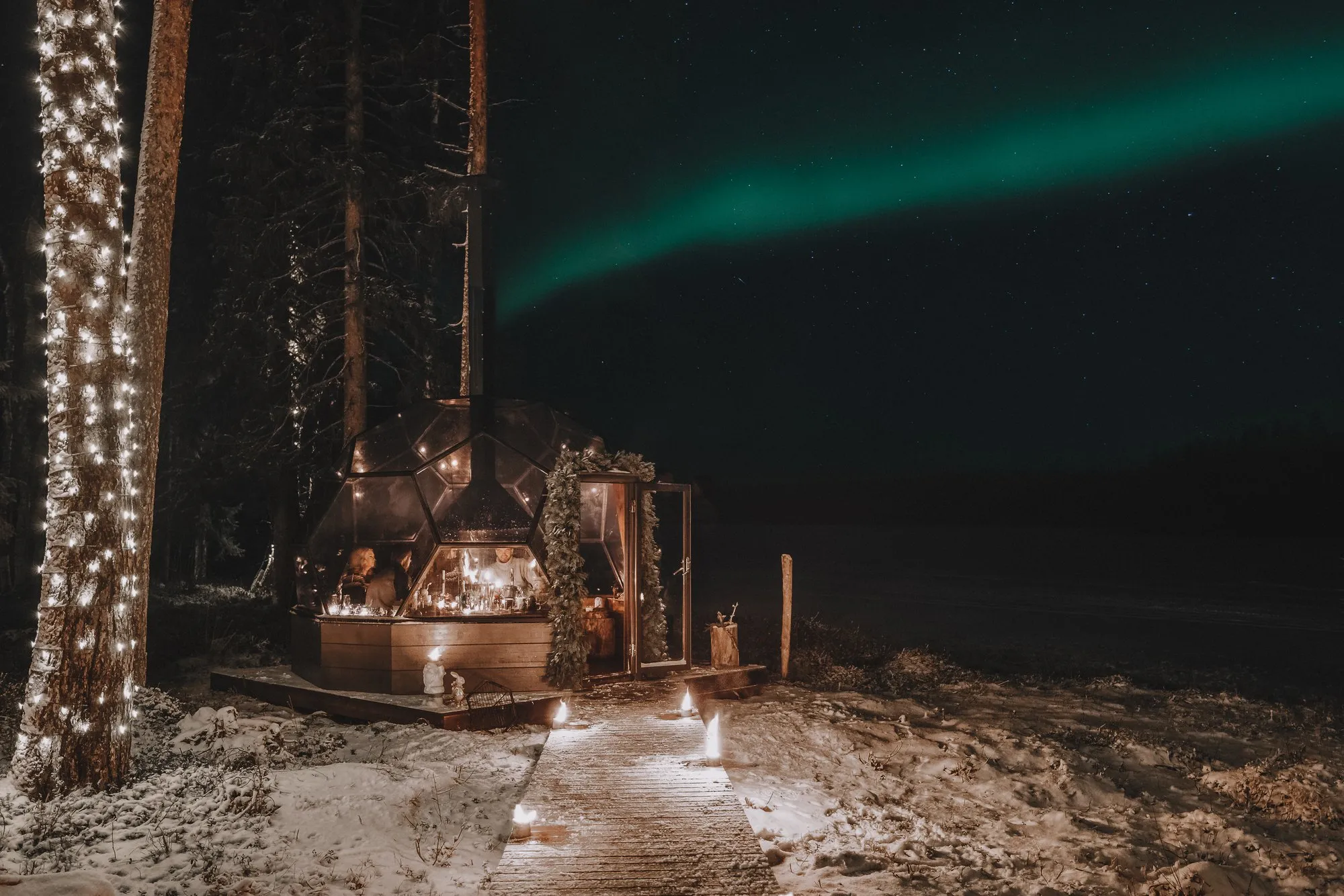 Candlelit glass dome hut in a snowy Lapland forest under the northern lights