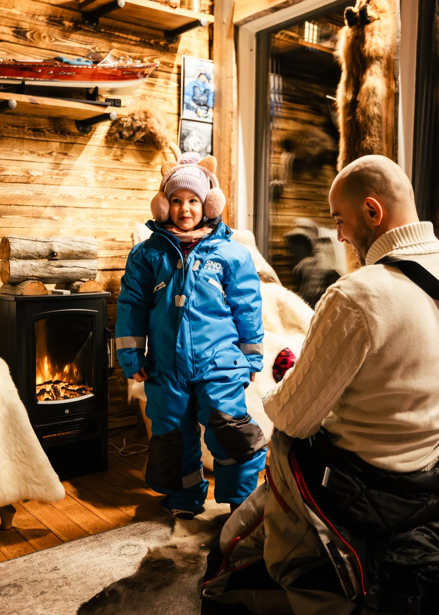 Smiling child in a blue snowsuit getting ready for a winter adventure in a Lapland cabin