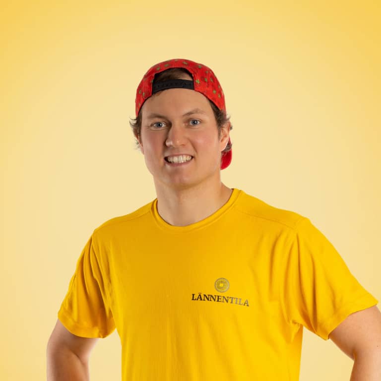 Nuori mies hymyilee kameralle, yllään punainen lippalakki takaperin ja keltainen t-paita, jossa on LÄNNENTILA-logo. Tausta on keltainen ja valaistus kirkas.