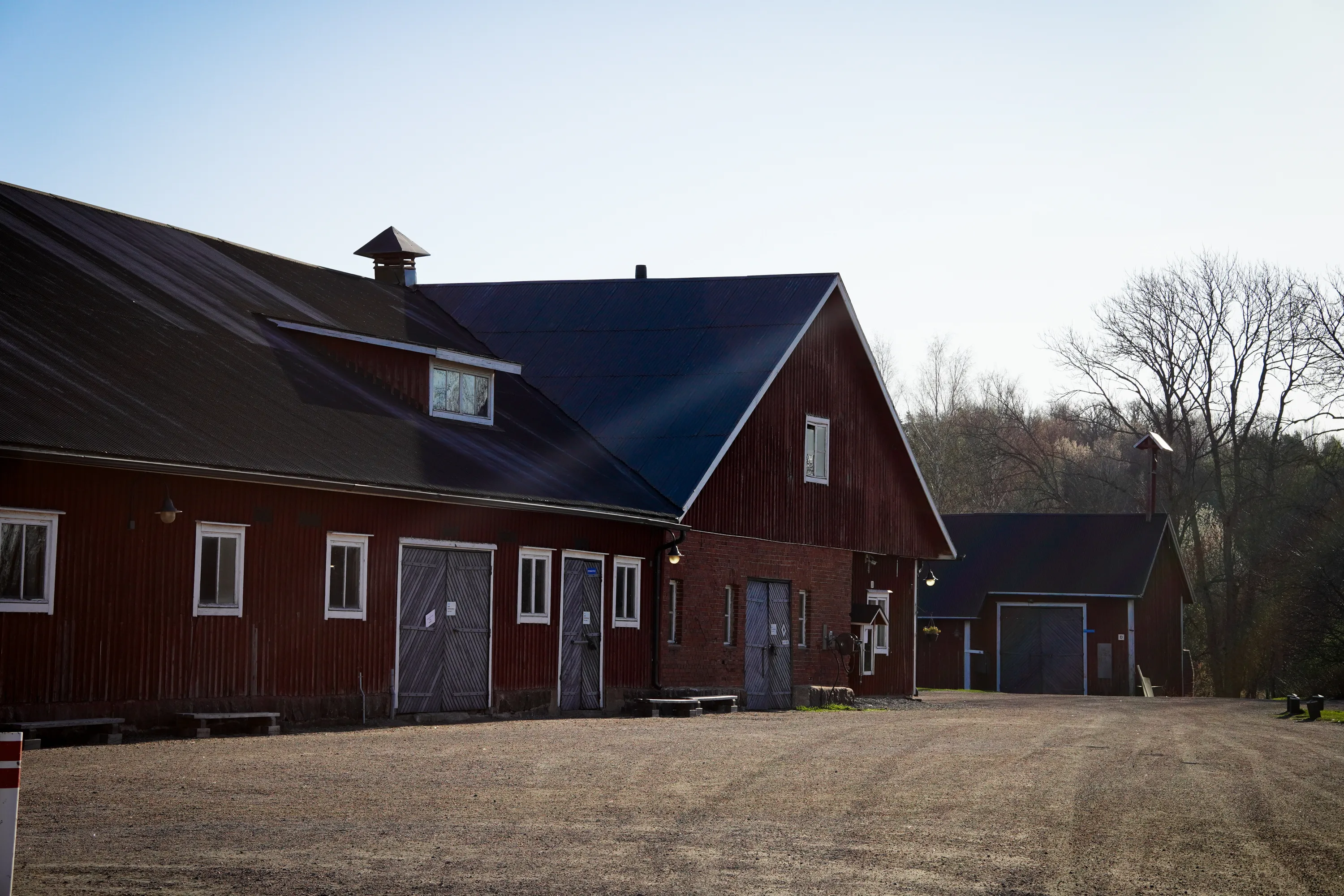 Useita punaisia ulkorakennuksia tummilla peltikatoilla aurinkoisena päivänä. Etualalla on laaja sorapiha. Rakennuksissa on valkoisia ikkunoita ja puisia ovia. Taustalla on lehdettömiä puita vaaleaa taivasta vasten. Vasemmanpuoleisen rakennuksen katolla on pieni kupu ja oikeanpuoleisen rakennuksen takana näkyy pieni kellotornimainen rakenne.