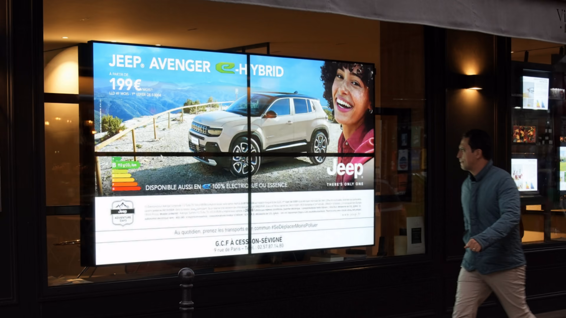 Affiche publicitaire Jeep Avenger e-Hybrid avec SUV beige et une femme souriante devant un paysage de montagne.