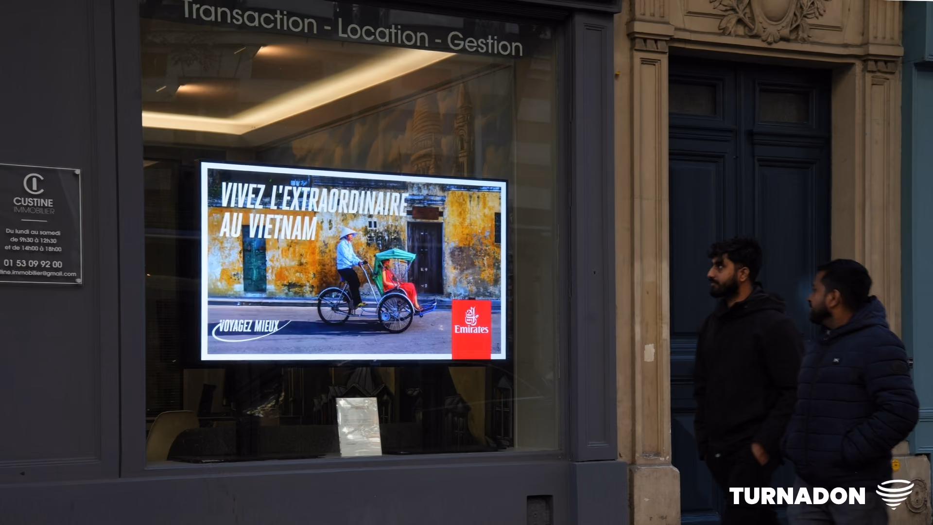 Deux hommes regardent une publicité pour Emirates montrant un cyclo-pousse au Vietnam.