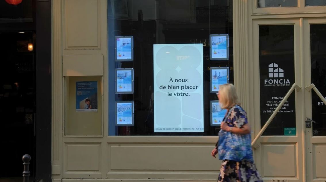 Une femme passe deant une vitrine et regarde l'écran pour voir la publicité Yomoni