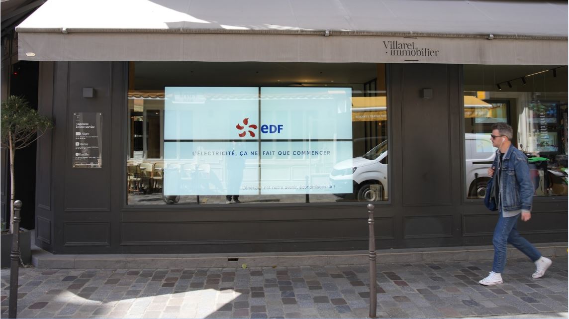 Un homme passe devant une vitrine et regarde lap ublicité affichée pour EDF