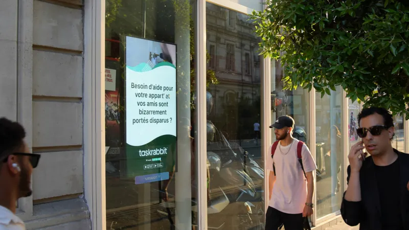 Personne utilisant son smartphone après avoir vu une publicité pour une application sur un écran d'affichage numérique.
