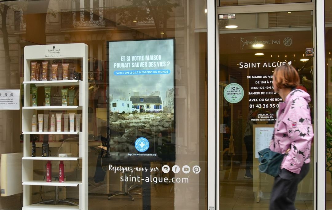 Une femme passe devant une vitrine et regarde l'écran digital diffusant une publicité pour une ONG