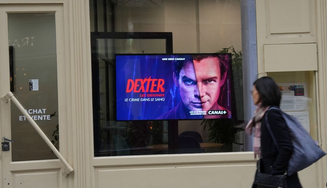 Une dame passe devant l'écran digital faisant la promotion de la série Dexter, sur Canal+