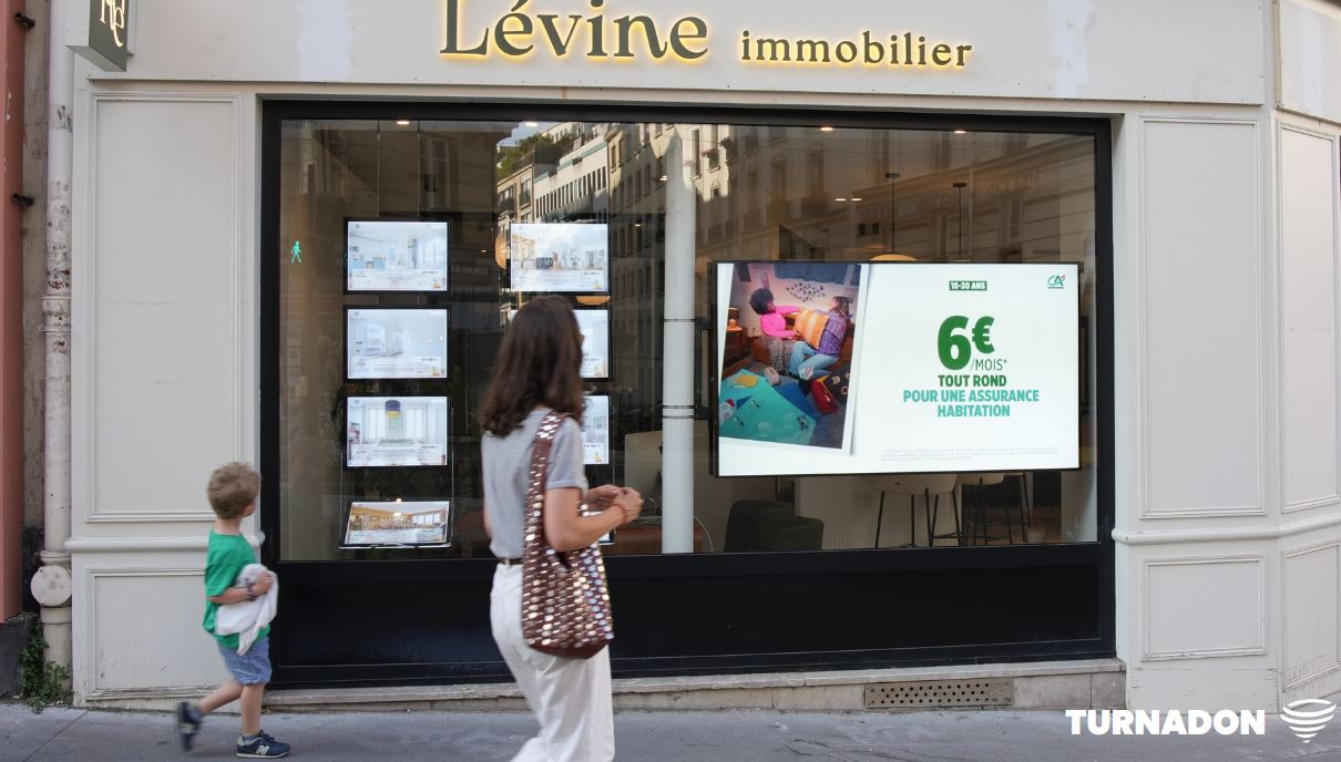 Une maan passe avec son petit fils devant un écran publicitaire faisant la promotion d'une offre pour Crédit Agricole