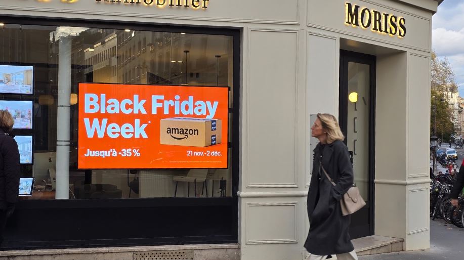 Une dame passe devant une vitrine en regardant l'écran publicitaire Amazon