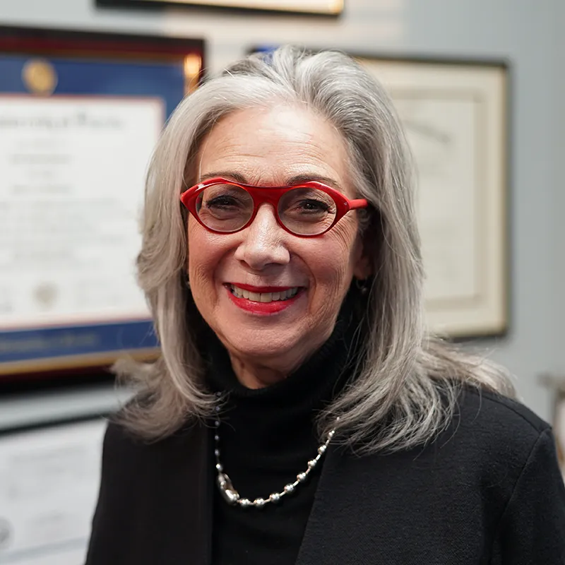 Smiling audiologist with headset and glasses adjusting controls on medical device in office.