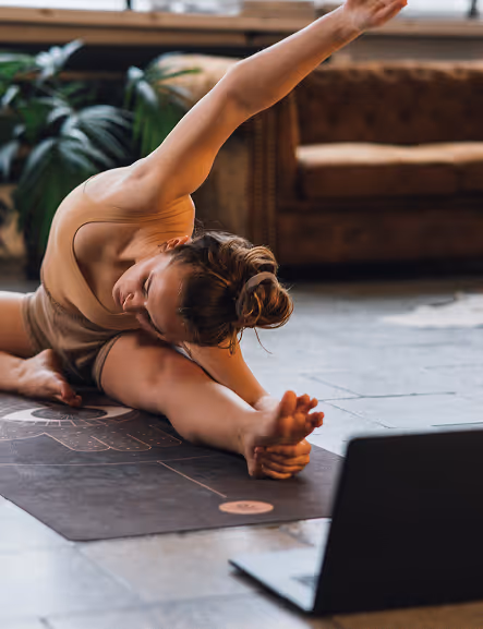 Frau übt seitliche Yoga-Dehnung auf Matte neben einem Laptop für Online Yoga bei Nalu Yoga Rostock