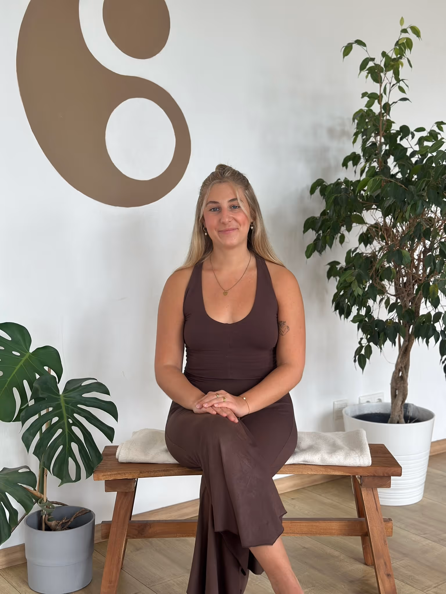 Lara, Yogalehrerin bei Nalu Yoga Rostock, sitzt lächelnd auf einer Bank im Studio vor dem Yin-Yang-Symbol