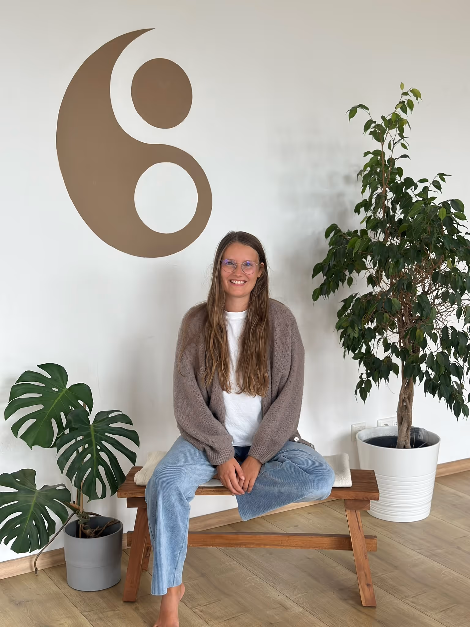 Lina, Inhaberin von Nalu Yoga Rostock, sitzt lächelnd auf einer Bank im Studio vor dem Nalu-Logo