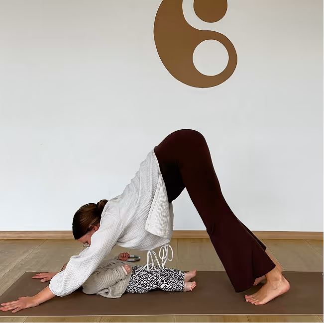 Mutter übt Herabschauender Hund vor ihrem Baby auf der Matte im Mama-Baby Yoga Kurs bei Nalu Yoga Rostock