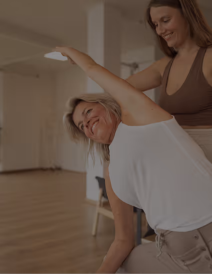 Yogalehrerin unterstützt lächelnde Schülerin bei seitlicher Dehnung im Studio von Nalu Yoga Rostock – Link zu 1:1 Yoga