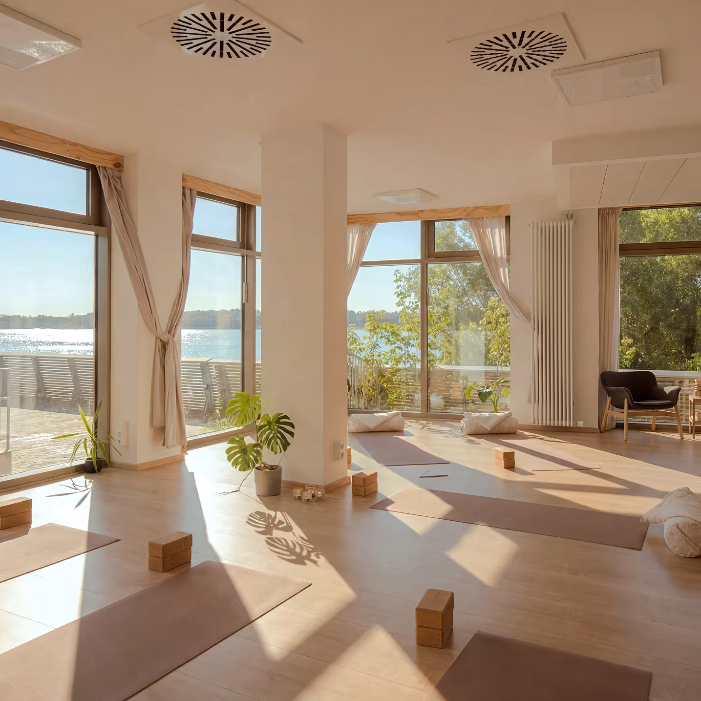 Sonnendurchfluteter Yogaraum mit Matten, Yogablöcken und großen Fenstern im Nalu Yoga Studio Rostock
