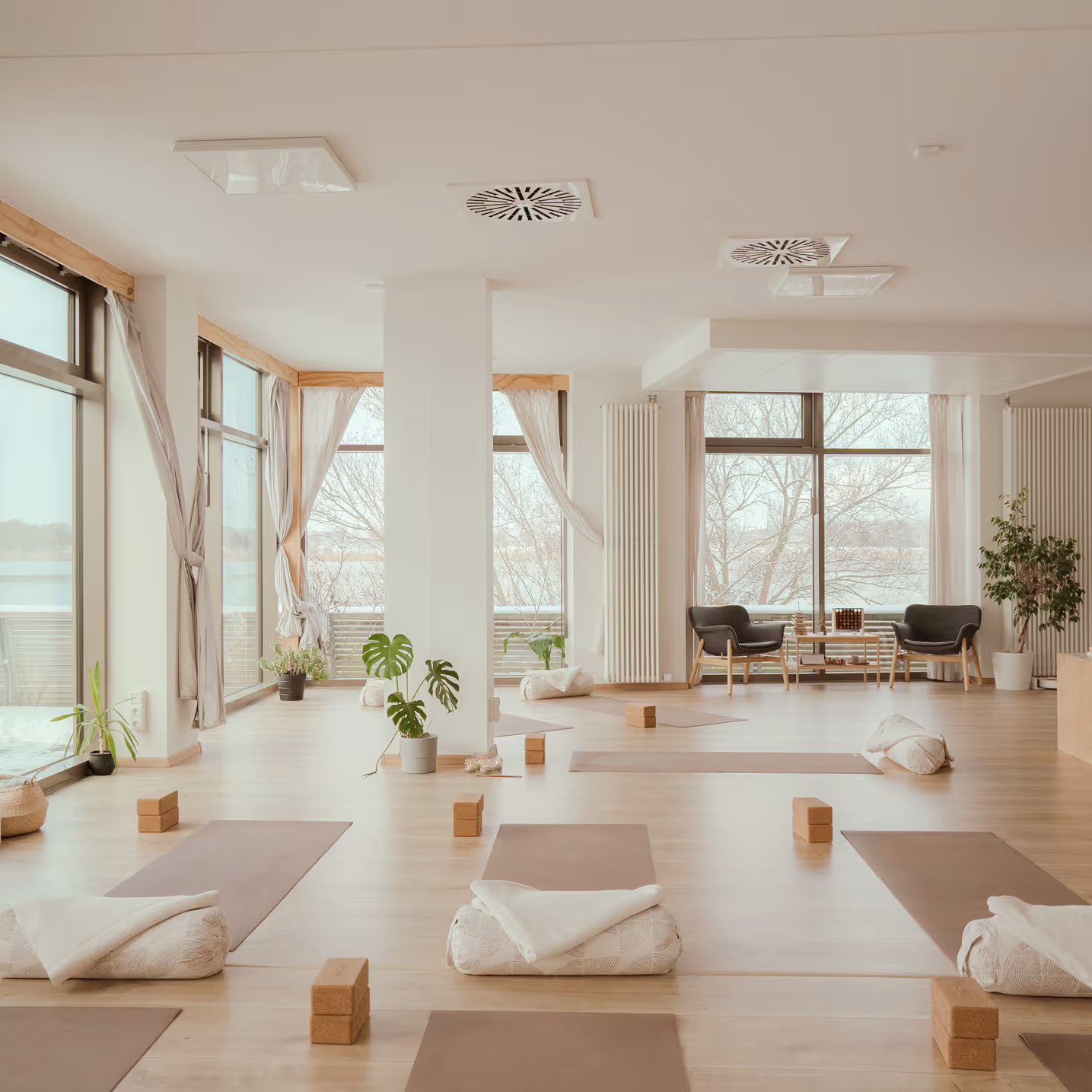 Weitläufiger Kursraum mit ausgelegten Yogamatten, Blöcken und großen Fenstern mit Blick auf die Warnow im Nalu Yoga Studio Rostock