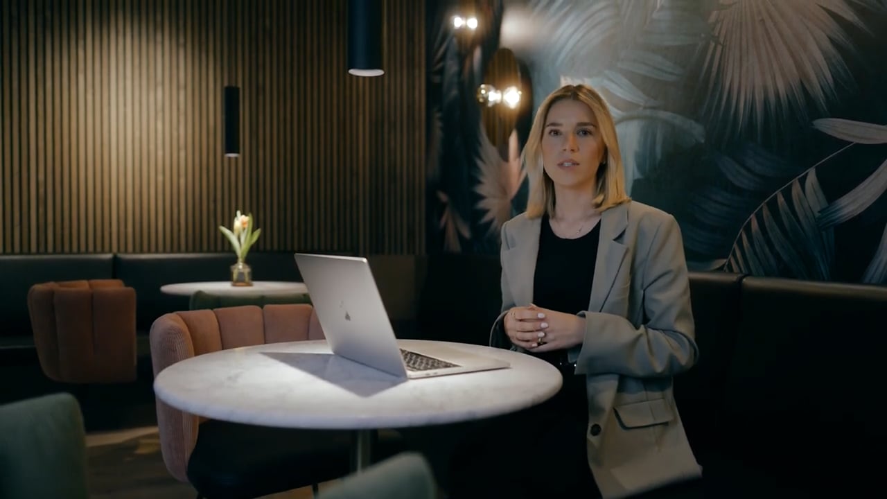 Frau sitzt an einem runden Tisch mit Laptop in modernem Café mit dunkler, gepolsterter Einrichtung.