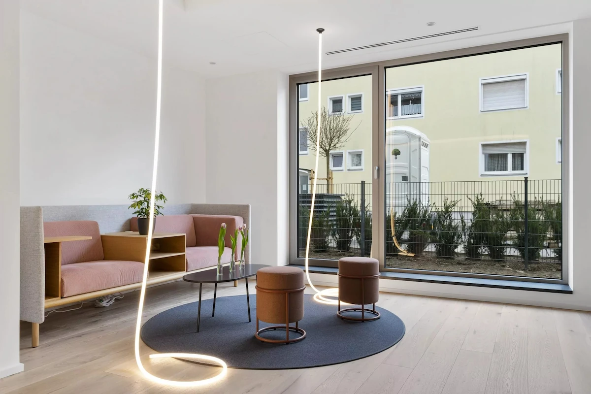 Moderner Sitzbereich mit rosa Sofa, zwei Hockern, rundem Teppich, Fenstern und Hängeleuchten.