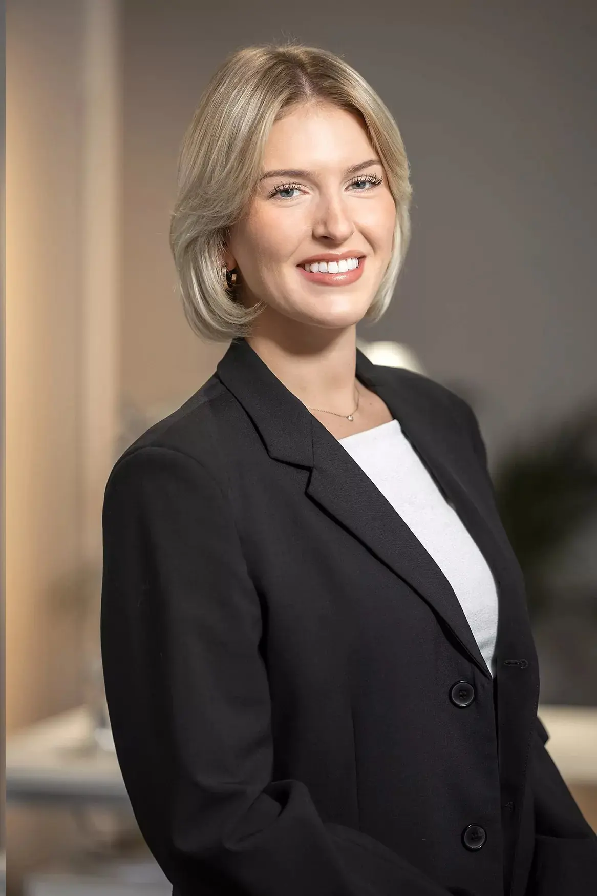 Porträt einer lächelnden Frau mit kurzem blondem Haar, die einen schwarzen Blazer trägt.