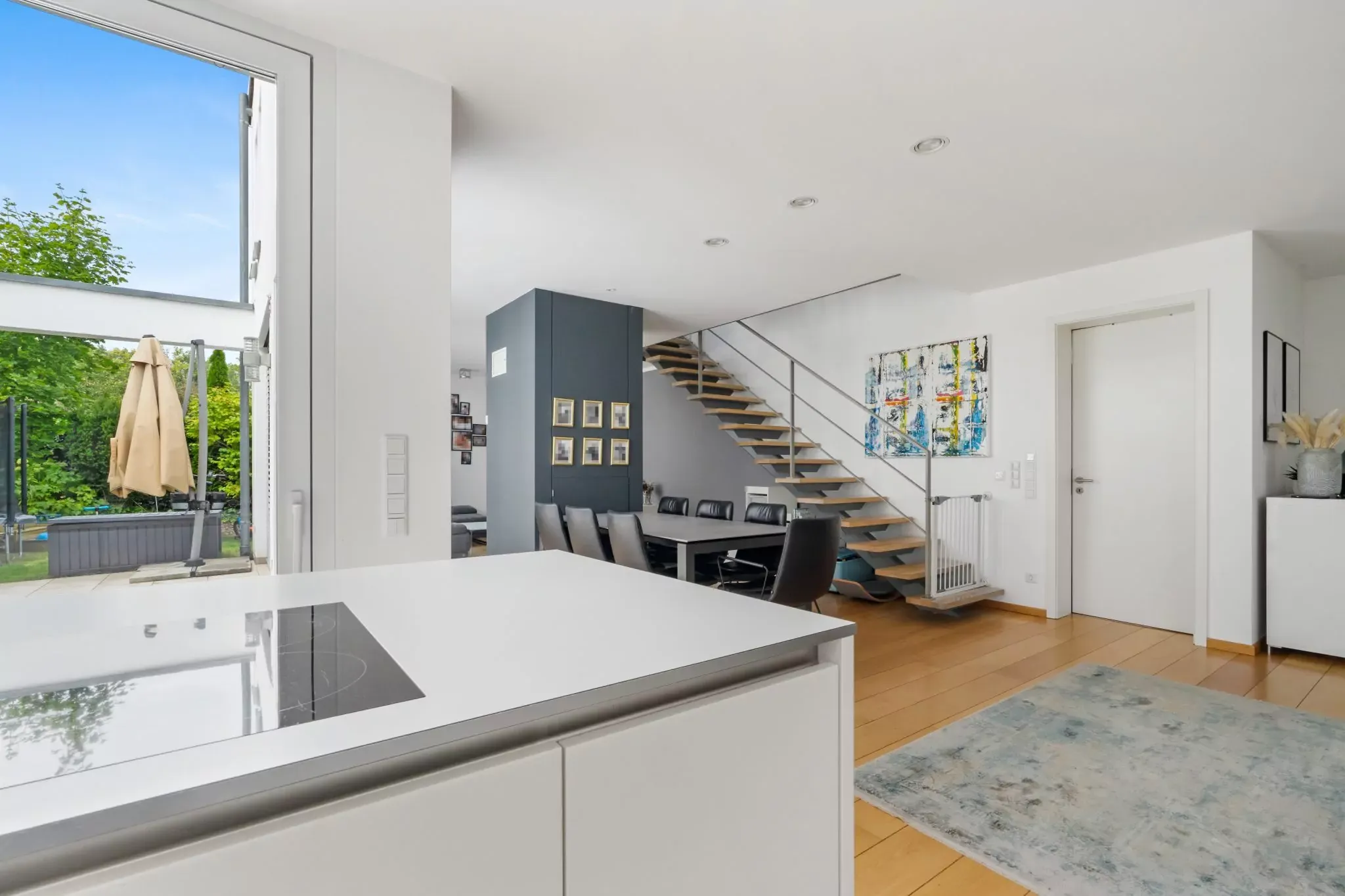 Moderner offener Wohnraum mit Küche, Holzboden, Treppe, Essbereich und Gartentür mit Blick ins Grüne.