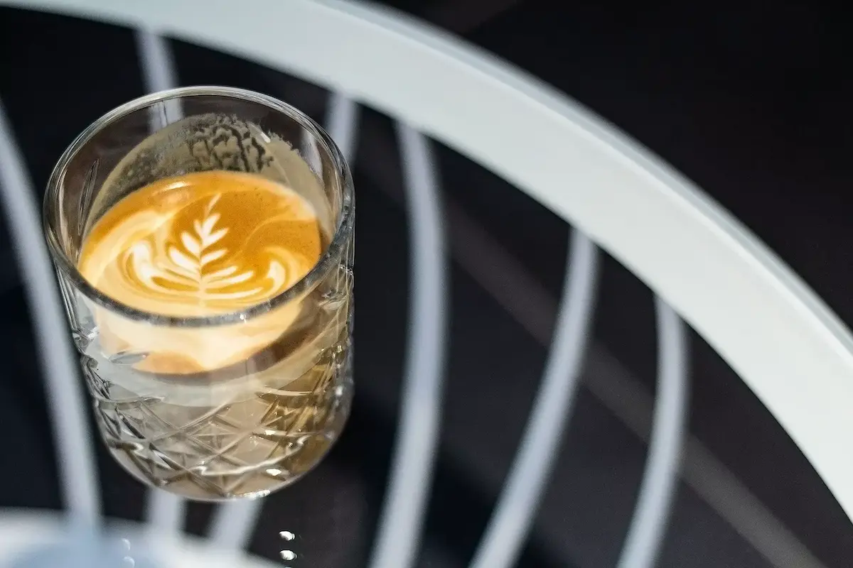 Ein Glas mit Latte Macchiato und Milchschaumkunst auf einem Glastisch.