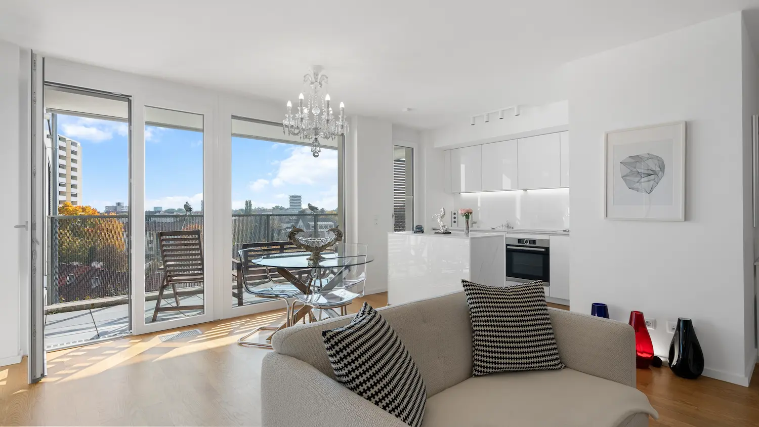 Helle, moderne Wohnung mit Glas-Schiebetüren, Balkon, Essbereich mit Glastisch und offener Küche.