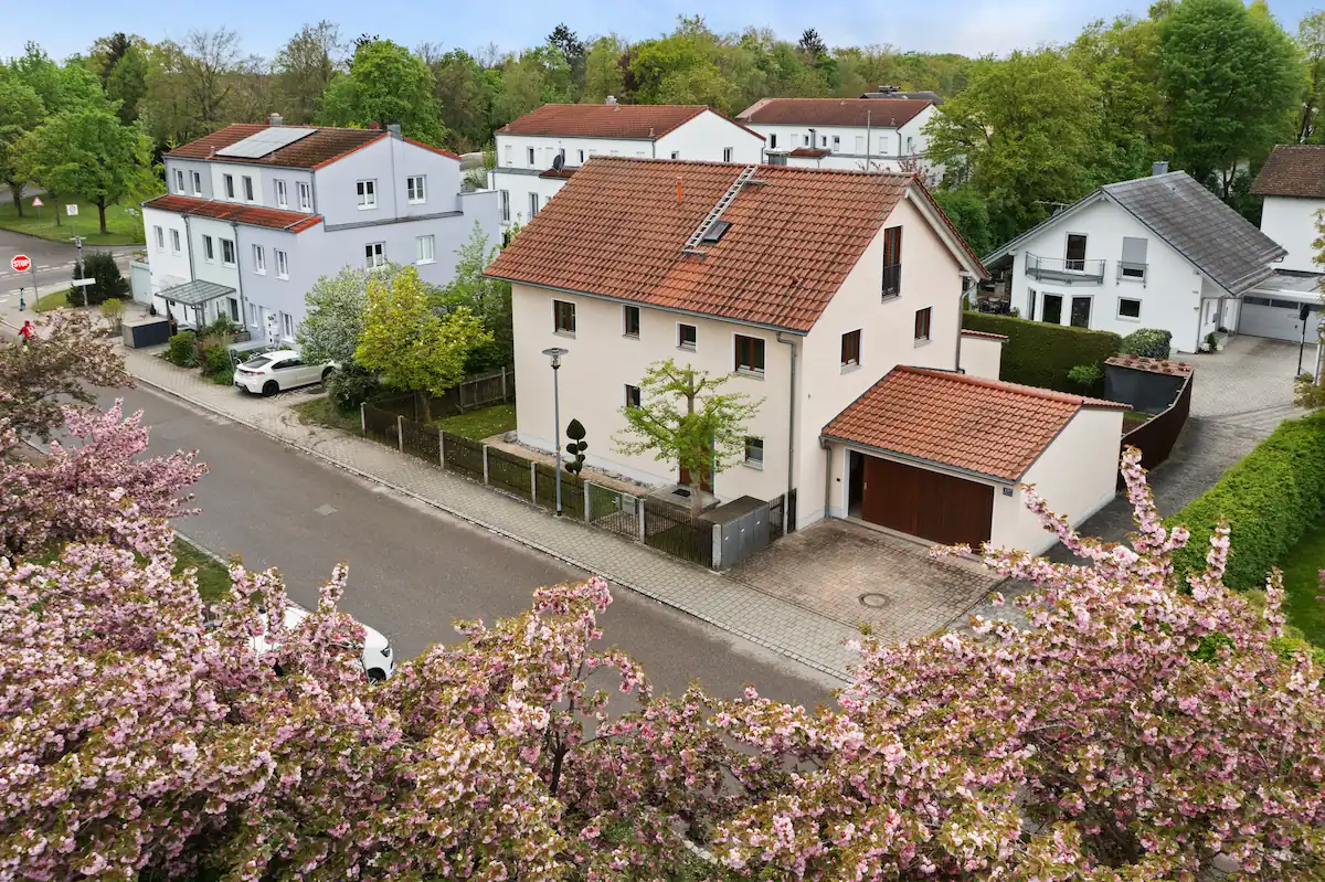 Blick auf ruhige Wohnstraße mit weißen Häusern, blühenden Bäumen und grünen Anlagen im Frühling.