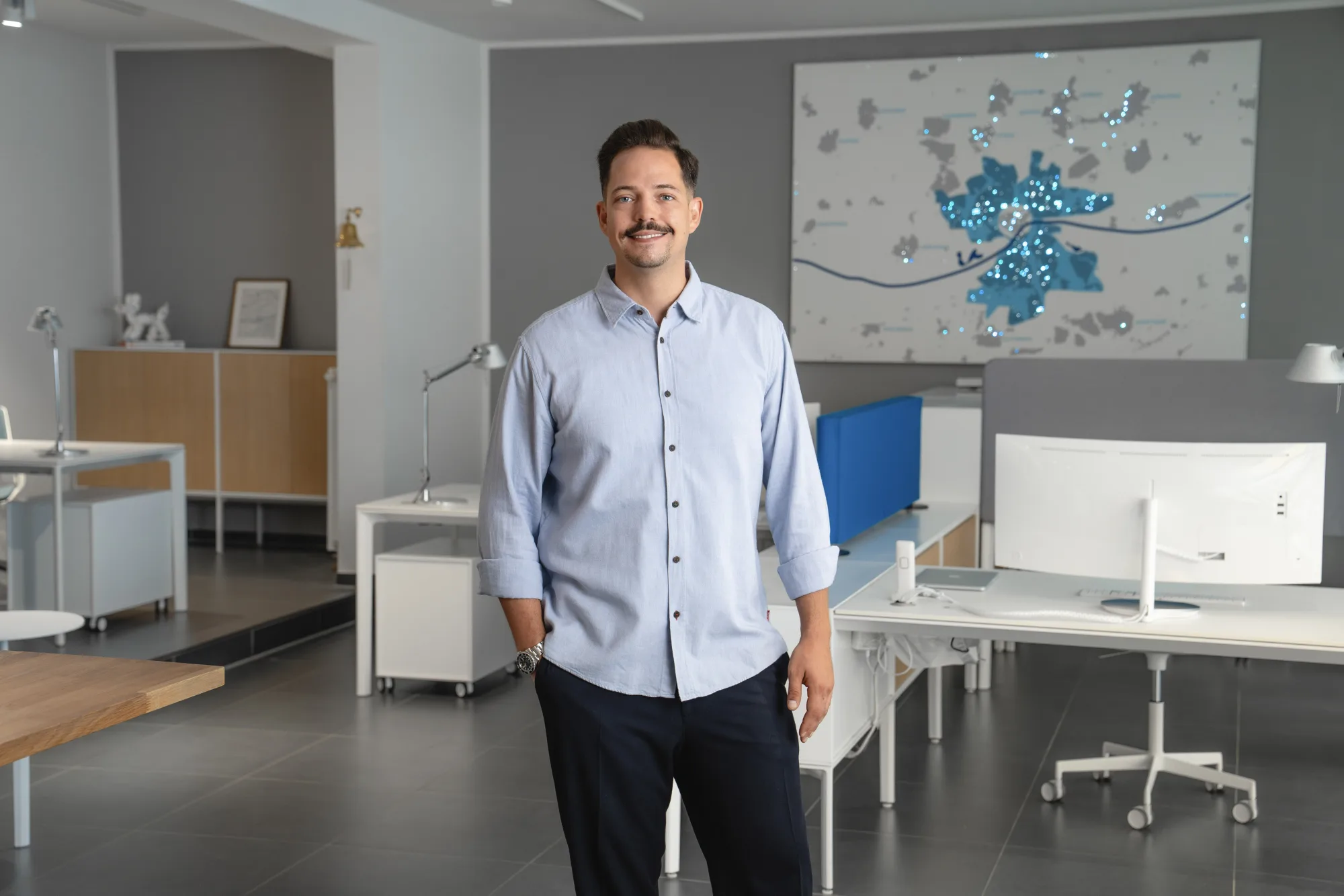 Mann mit Schnurrbart in weißem Hemd schaut mit gefalteten Händen in die Kamera.