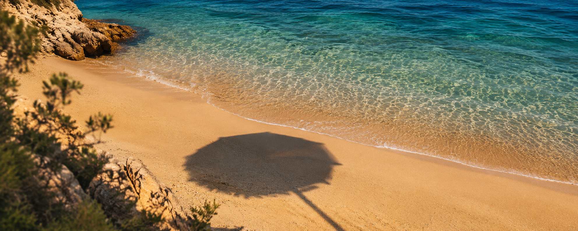 Sombras de una sombrilla en arena dorada junto a agua cristalina azul en una playa rocoso