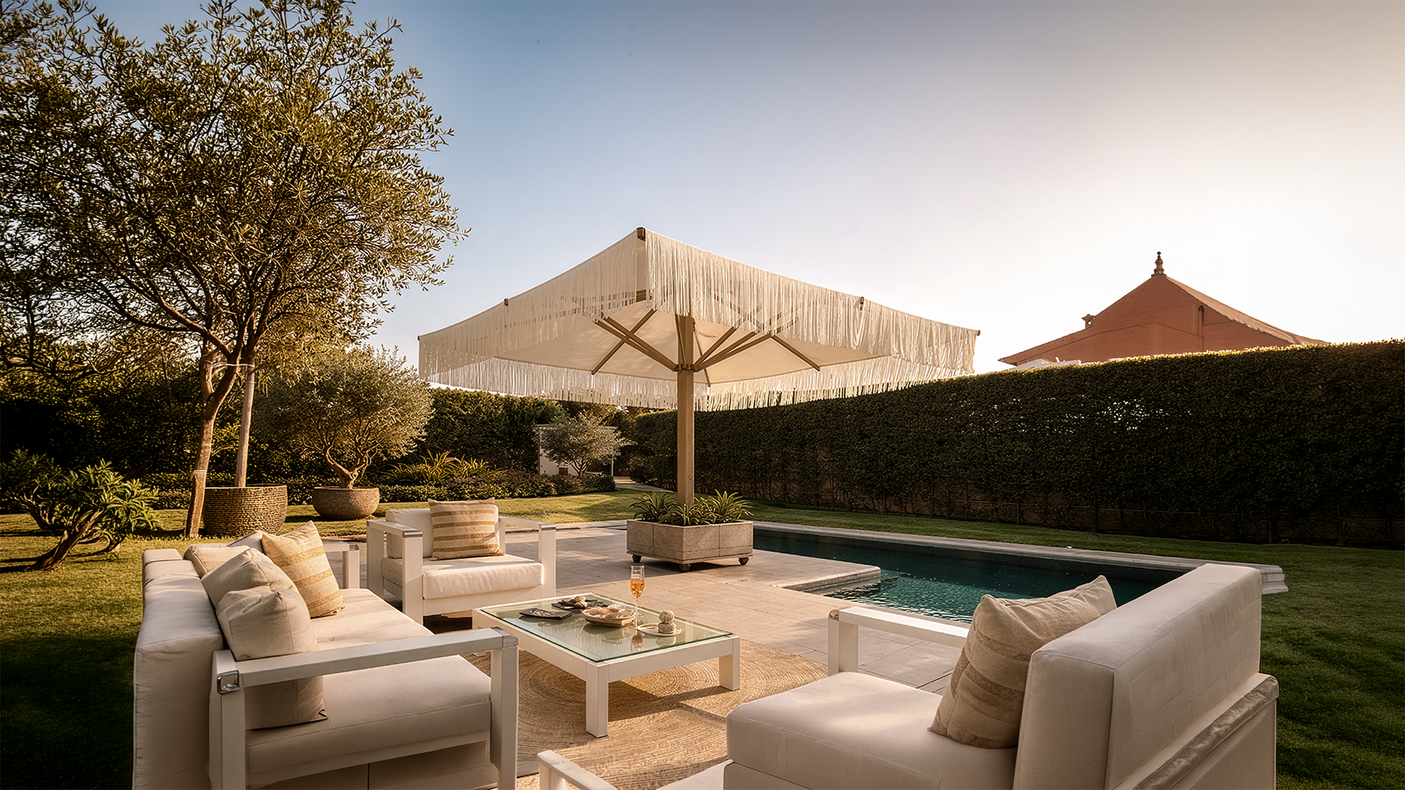 Zona exterior con sofá y sillones beige junto a una piscina y sombrilla grande con flecos.